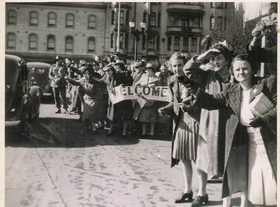 Crowd scene with 'WELCOME' banner, women waving, city street, Melbourne, c.1945 — Bob Webber homecoming welcome