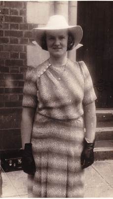 Lil Webber Rowe in wide-brimmed white hat and striped dress with black gloves, standing outside a brick building, c.1930s–1940s