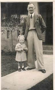 Robertson/Webber family — tall man with a small girl standing on a path outside a brick building, c.1940s–1950s