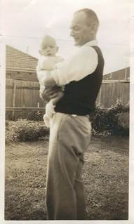 Robertson/Webber family man holding a baby in a suburban backyard, timber fence behind, c.1940s–1950s