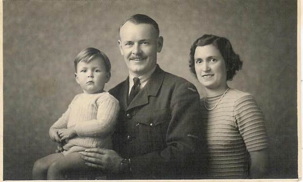 Studio portrait: officer in military uniform with toddler and wife, c.1940s — formal studio photograph, man in uniform seated or standing with young child and woman
