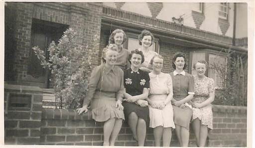 Robertson/Webber family — group of seven women seated and standing on a low brick wall outside a brick building, c.1940s–1950s