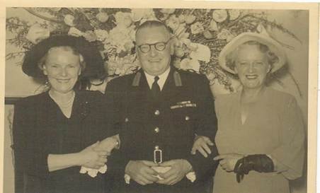 Robertson/Webber family — two women and a man in dark uniform, floral backdrop, formal occasion, c.1950s–1960s