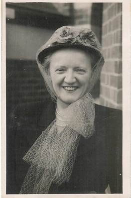 Robertson/Webber family woman in hat with net veil, smiling broadly, brick wall behind, c.1940s