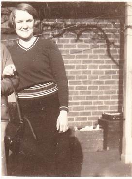 Woman in V-neck striped jumper leaning against a brick wall, c.1930s — informal outdoor portrait